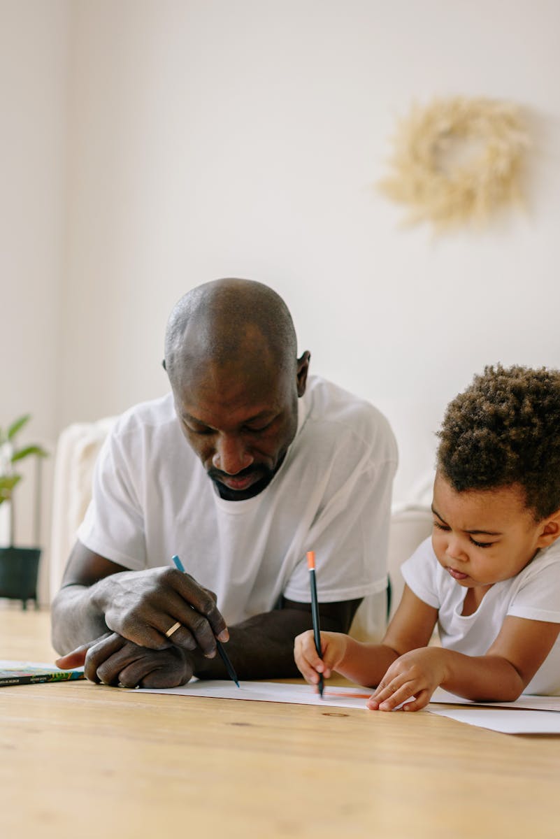 Heartwarming scene of a father and son drawing together on a wooden floor at home.